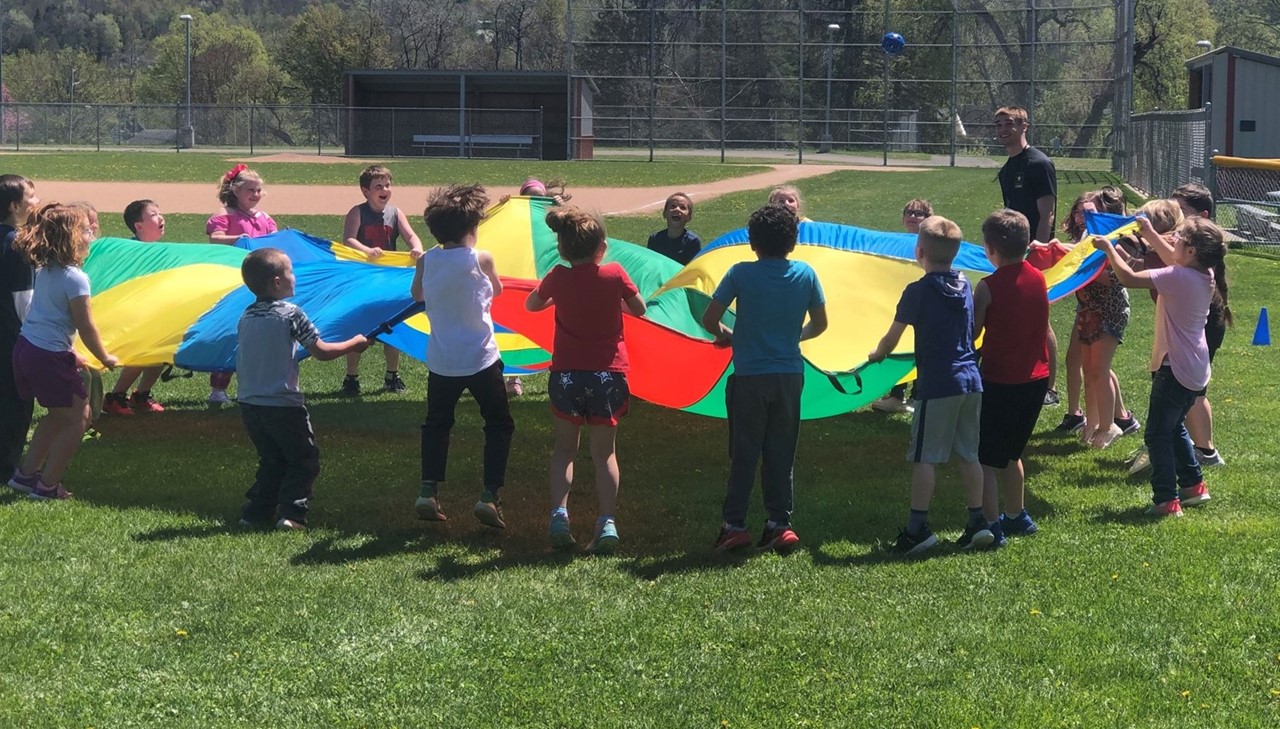 primary school children playing with a large rainbow tent outside
